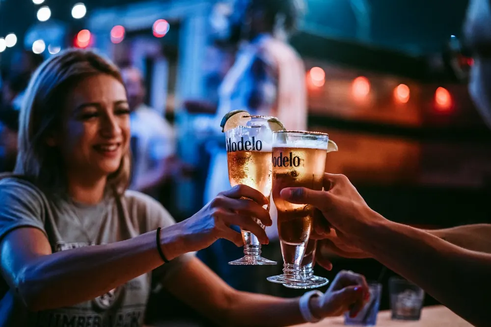 Três pessoas brindando com cerveja num bar
